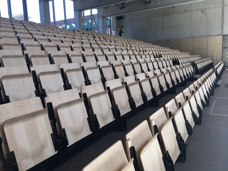 Auditorium met volautomatische uitschuifbare tribune aangedreven door duwkettingsyteem. Collegezaalstoelen COS essential wood. Scholencomplex Don Bosco Haacht.