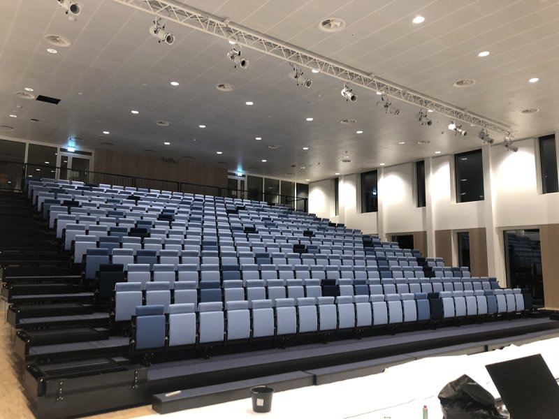 Uitschuifbare of telescopische tribune, volledig automatische stoelrijen, aangedreven door duwkettingsysteem. Auditorium hoofdkantoor Hempel SA te Lyngby Denemarken. 